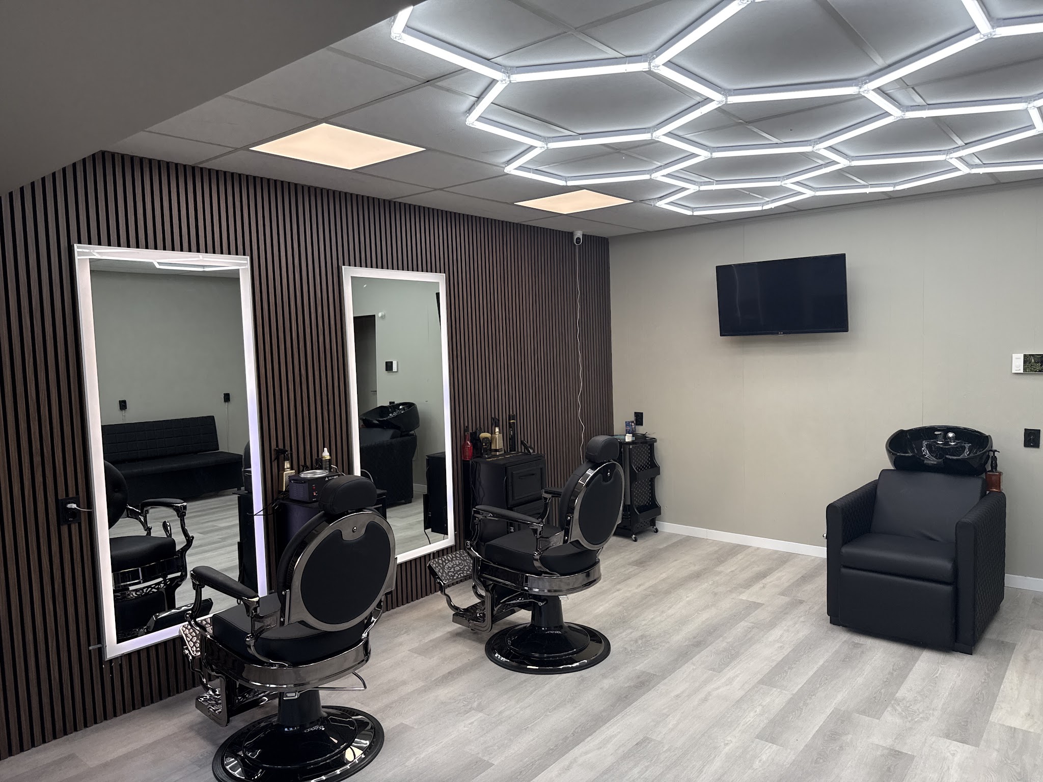 Interieur van Number one Barbershop: twee zwarte barbierstoelen, twee spiegels met ledrand, een wasbak, een wand van donkere houten lamellen en een plafond van lichtgevende zeshoeken