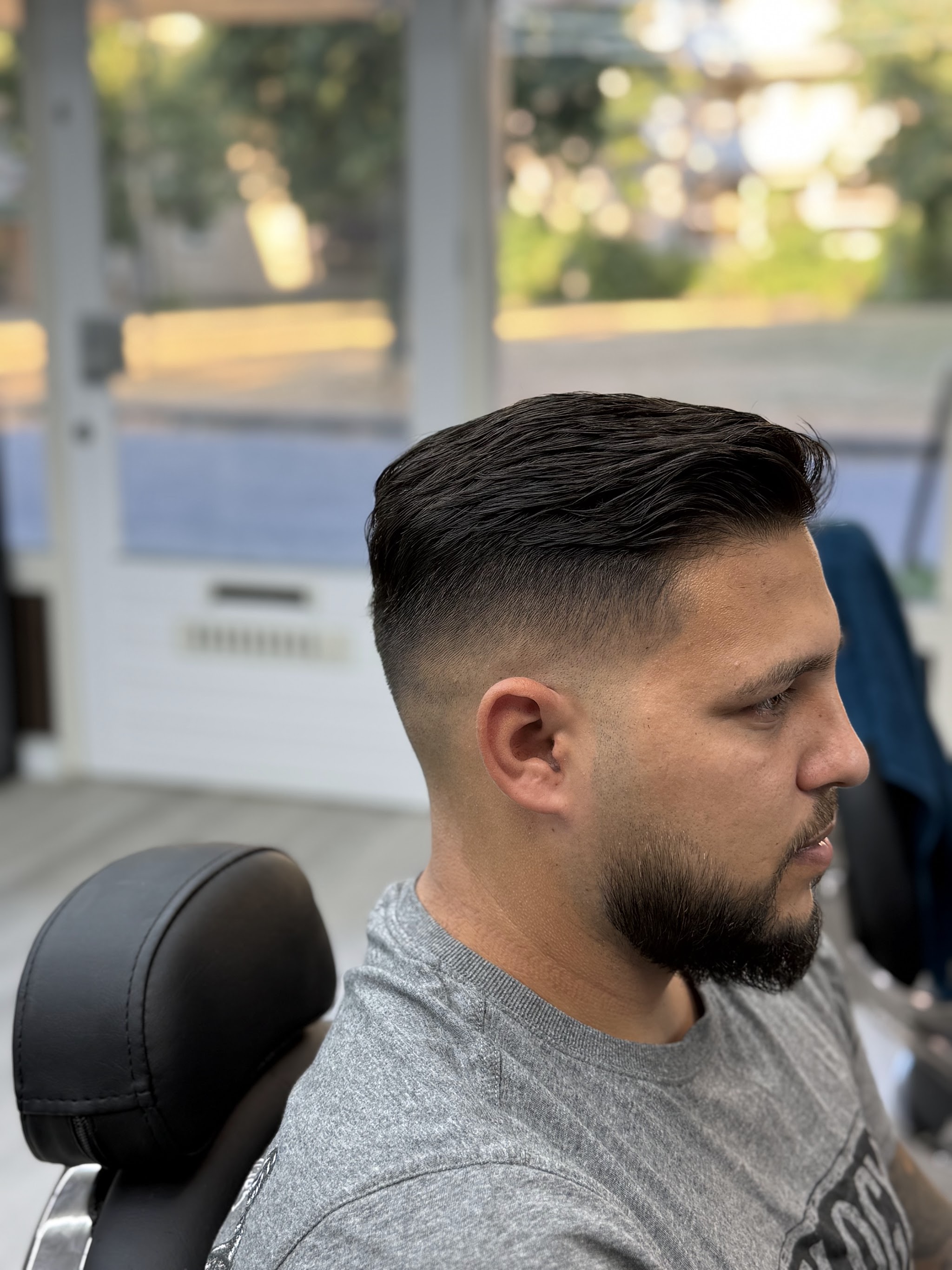 Klant met een bijgewerkte baard en een korte fade, van opzij in de barbierstoel
