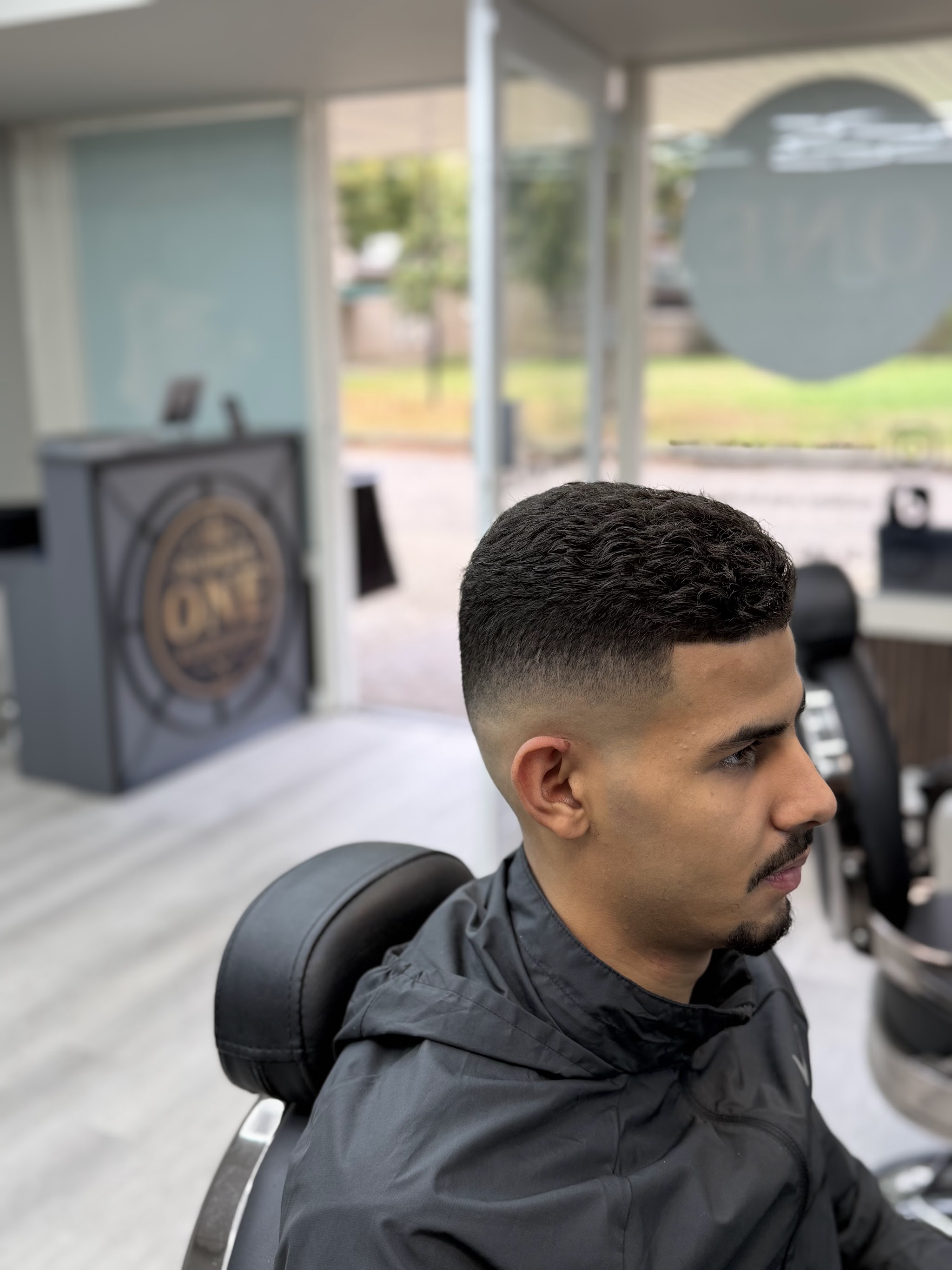 Verse skin fade bij Number one Barbershop, met de balie met het Number one-logo op de achtergrond